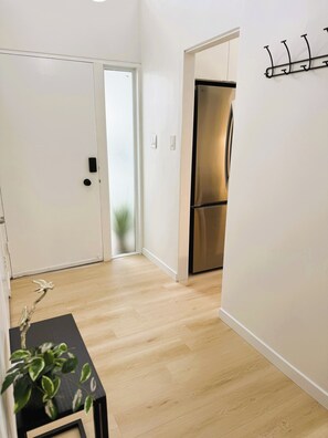 A hallway with a wooden floor, a stainless steel refrigerator, a white door, and a wall-mounted hook. - Modern Palo Alto Home -Perfect for Mid‑Term Stay (Palo Alto)