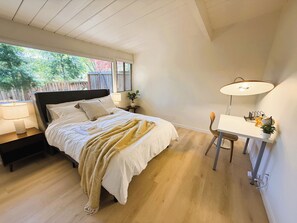 A bedroom with a bed, bedside tables, a desk with a chair, a lamp, and a window with a view of trees. - Modern Palo Alto Home -Perfect for Mid‑Term Stay (Palo Alto)