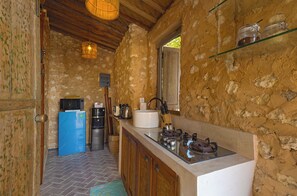 Una cocina rústica con pared de piedra, armarios de madera, un refrigerador azul, estufa a gas y una lámpara colgante.