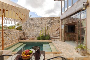 Un espace piscine avec des murs en pierre, une table garnie de fruits et de verres, et une chaise.