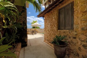 Un bâtiment en pierre avec une fenêtre et une porte, une terrasse avec une table et des chaises, et des plantes en pot.