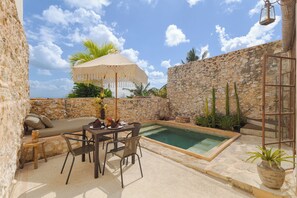 Un espace piscine comprenant une table et des chaises, un coin salon avec des coussins et un mur en pierre.