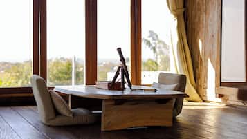Una mesa de madera con un trípode y una caja, dos sillas y vistas amplias a través de grandes ventanales.