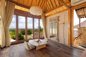 Una habitación con amplios ventanales, techo de madera y una mesa con cojines.