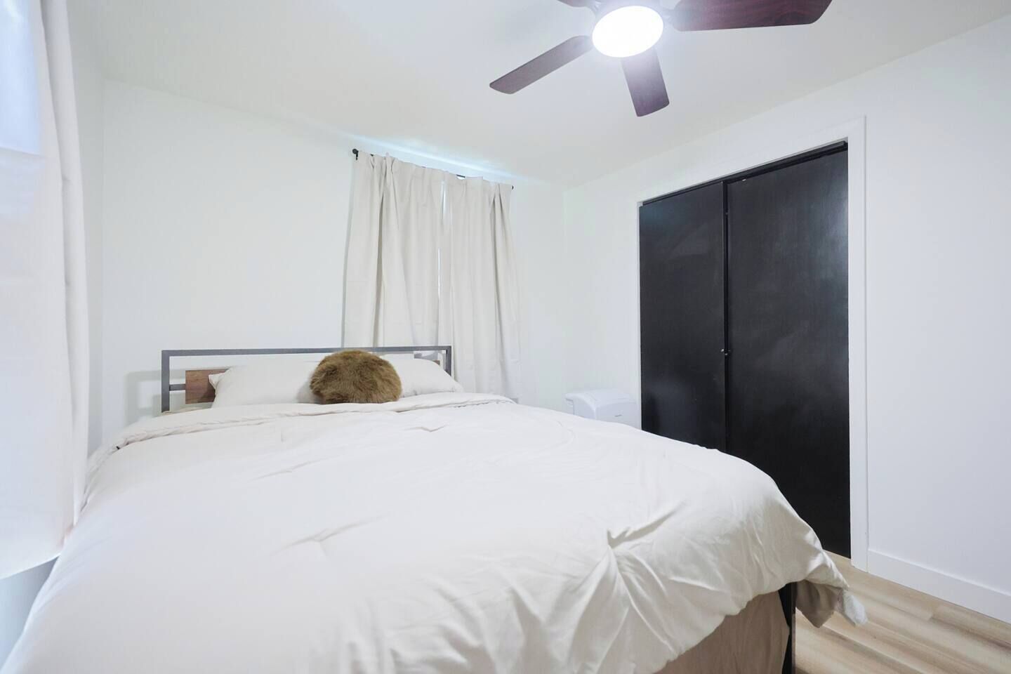 A bedroom with a bed, a ceiling fan, a black wardrobe, and a window with curtains.