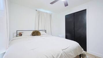 A bedroom with a bed, a ceiling fan, a black wardrobe, and a window with curtains.