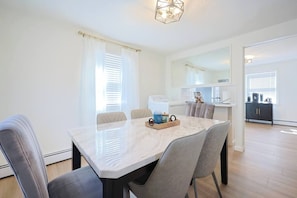 Een moderne eetruimte met een marmeren tafel, grijs gestoffeerde stoelen en een keuken op de achtergrond.