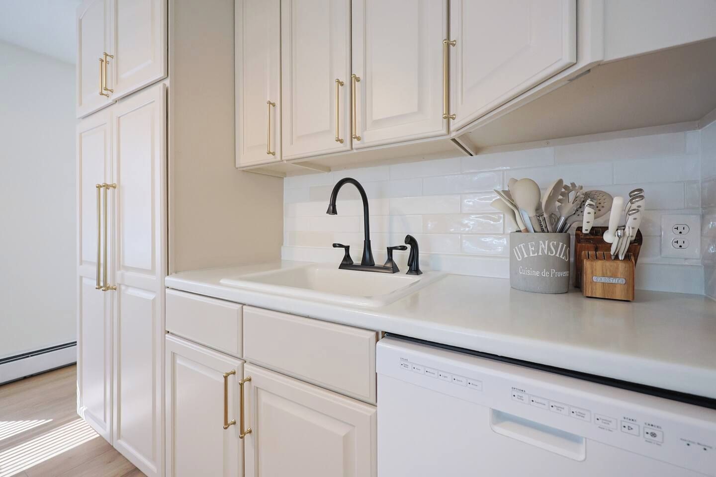 A kitchen with white cabinets, a black faucet, and a dish rack with utensils.