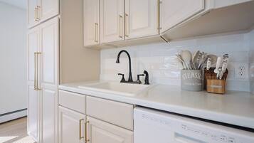A kitchen with white cabinets, a black faucet, and a dish rack with utensils.
