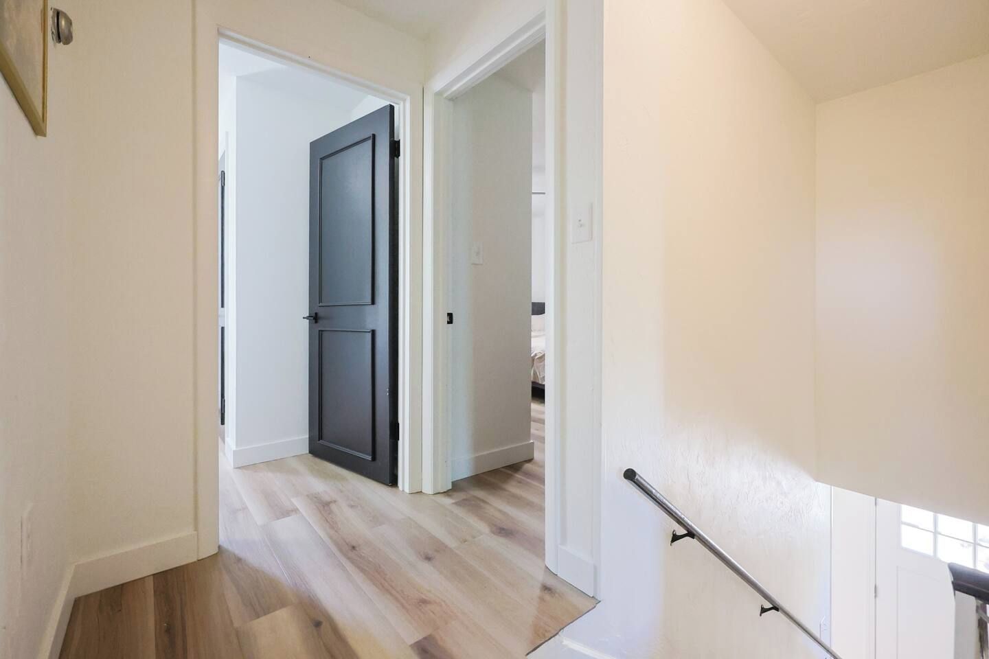 A hallway with a wooden floor, a dark door, and a white wall.