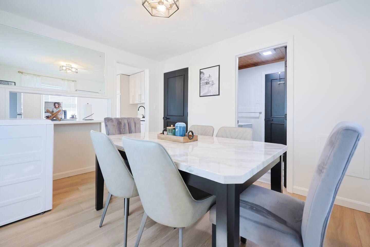 Une cuisine moderne avec des meubles blancs, un coin repas doté d’une table en marbre et de quatre chaises, et un couloir avec une porte.