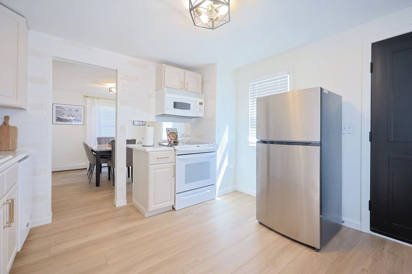 A modern kitchen with white cabinetry, a stainless steel refrigerator, and a dining area with a table and chairs.