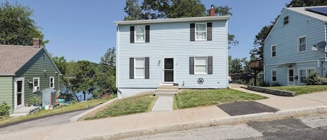 A two-story residential building with a front porch, a satellite dish, and a small front yard.