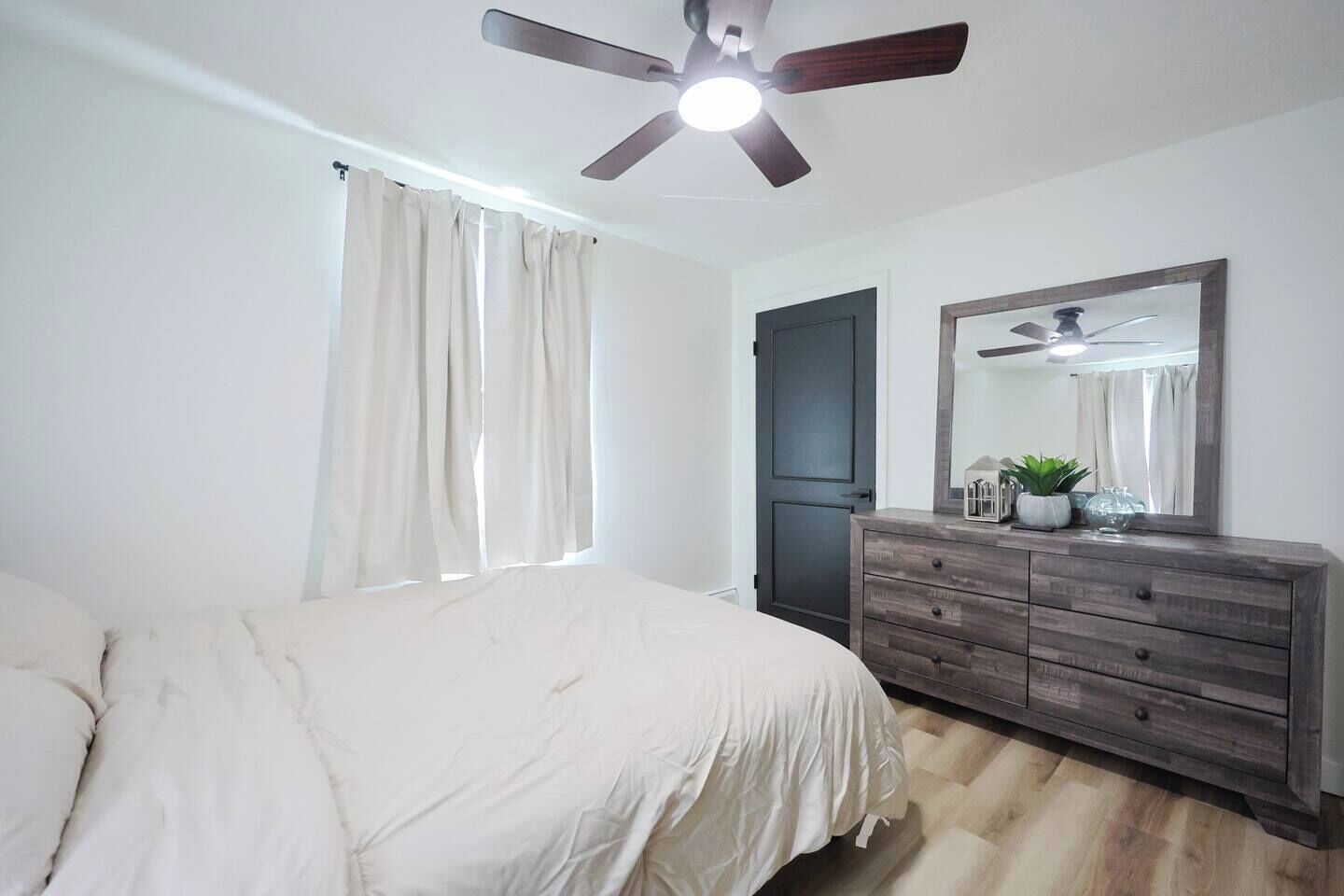 Ein Schlafzimmer mit einem Bett, einem Schminktisch, einem Deckenventilator und einem Fenster mit Vorhängen.