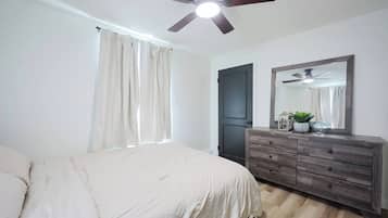 Ein Schlafzimmer mit einem Bett, einem Schminktisch, einem Deckenventilator und einem Fenster mit Vorhängen.
