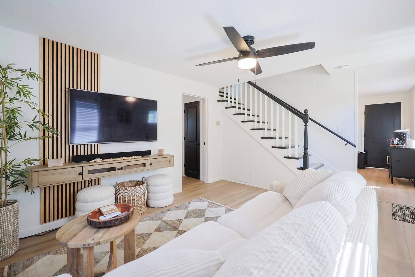 A modern living room with a flat-screen TV, a sofa, a coffee table, and a staircase.