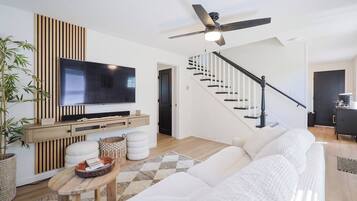 A modern living room with a flat-screen TV, a sofa, a coffee table, and a staircase.