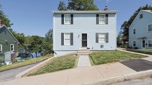 A two-story residential building with a front porch, a visible chimney, and a small front yard. - Renovated Lakefront 5BR • Near Colleges • Sunsets • Sleeps 12 (Worcester)