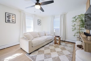 A modern living room with a sofa, a small table, and a ceiling fan. - Renovated Lakefront 5BR • Near Colleges • Sunsets • Sleeps 12 (Worcester)