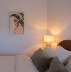 Ein Schlafzimmer mit einem Bett, Kissen, einer Nachttischlampe und einem Wandbild.