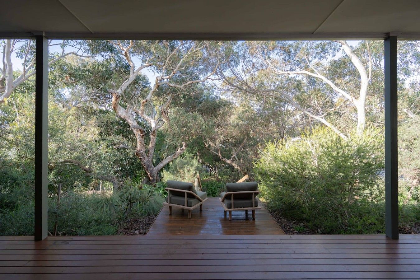 A covered outdoor area with two wooden chairs facing a natural landscape.