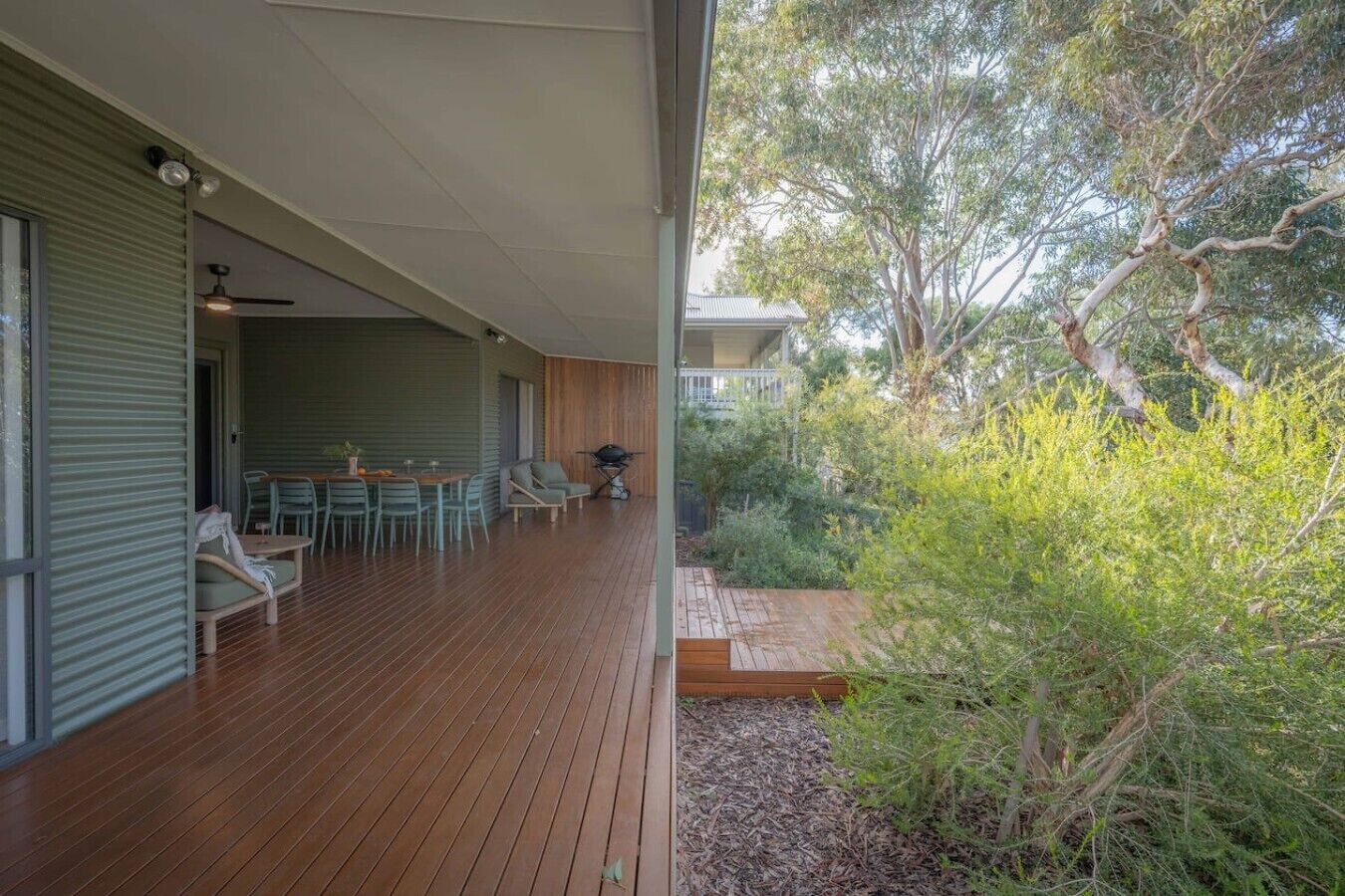 A covered outdoor area with a wooden deck, seating, and a barbecue grill.