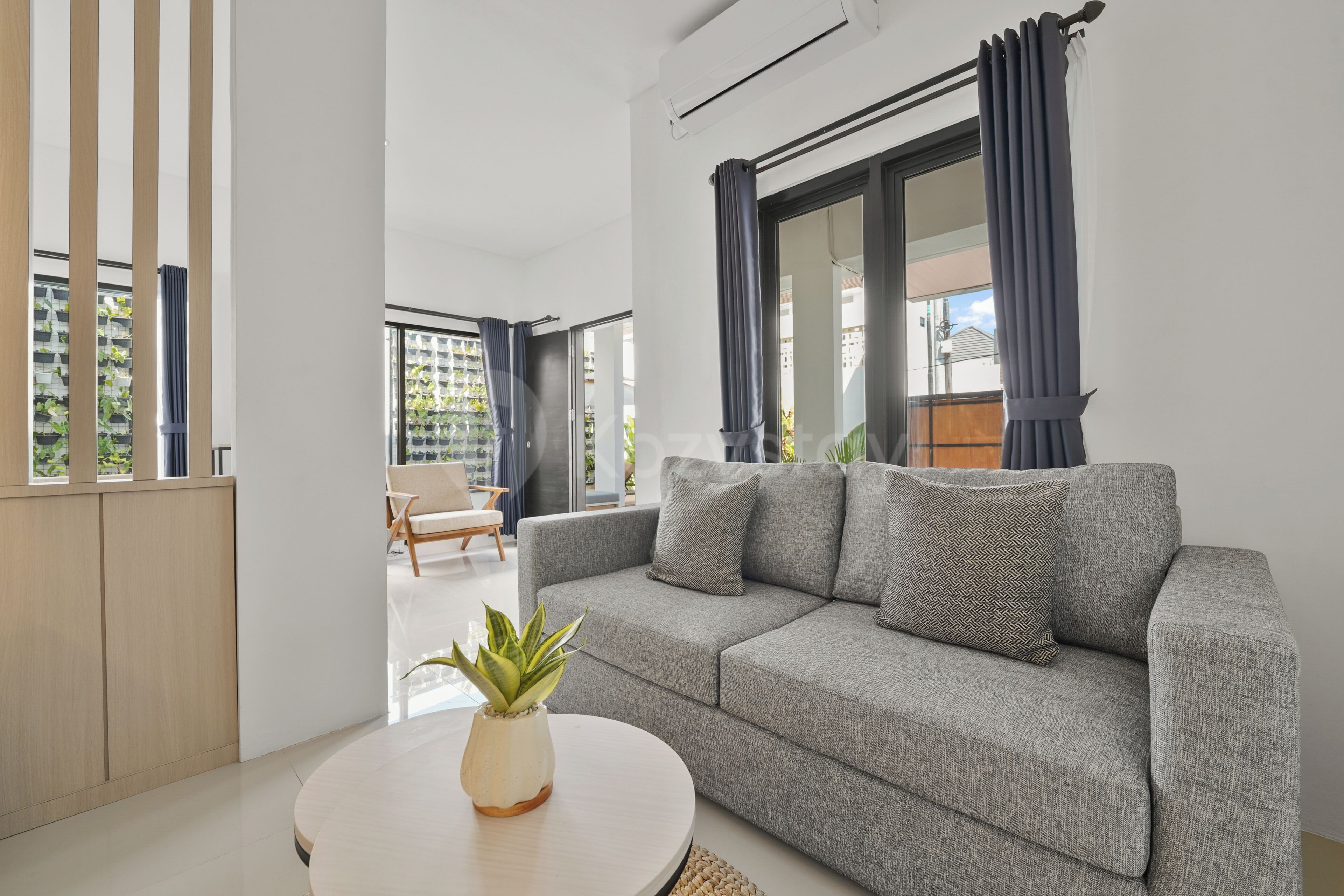 Ein modernes Wohnzimmer mit einem grauen Sofa, einem runden Couchtisch und einer Topfpflanze.