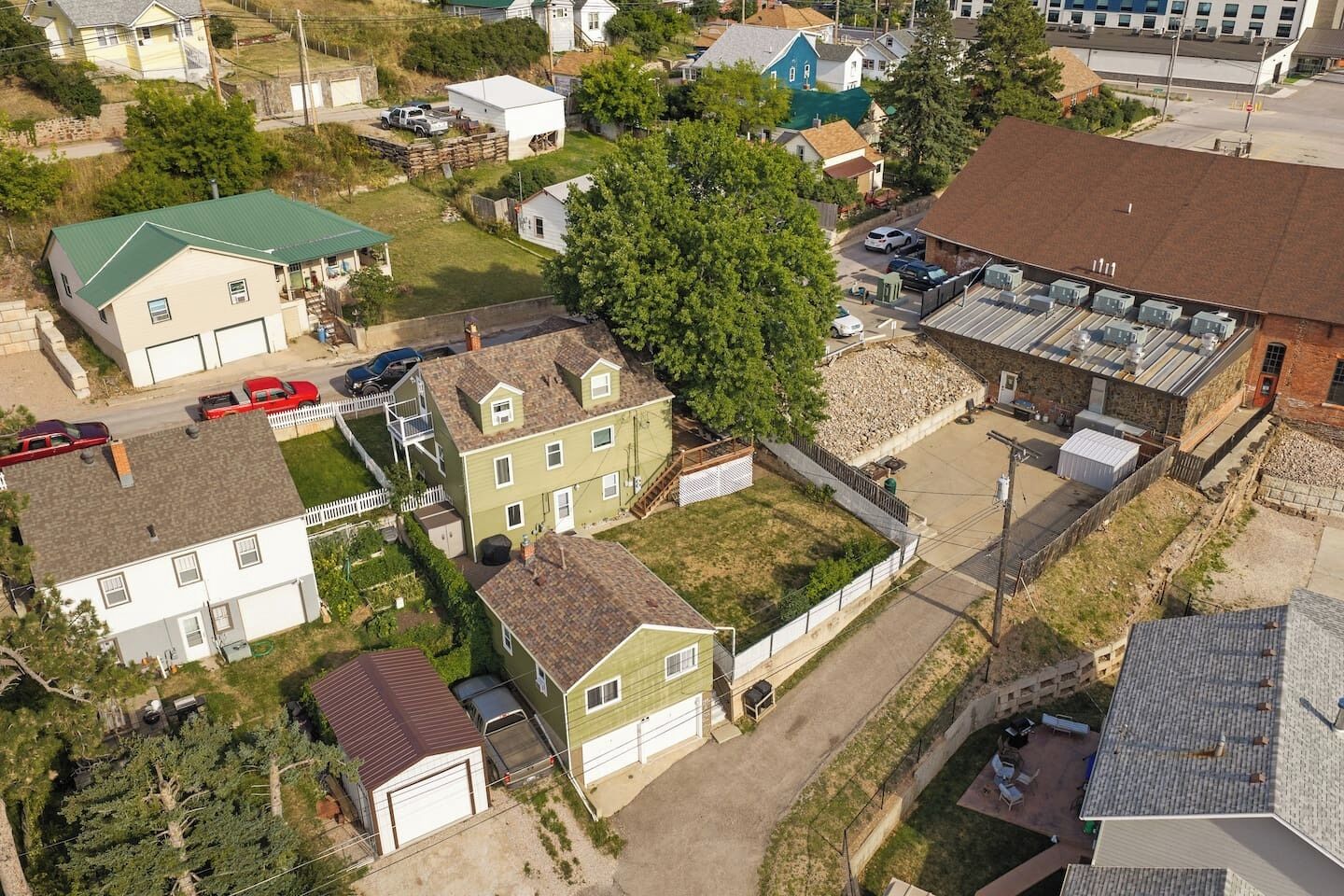 Vue aérienne d’un quartier résidentiel avec des maisons, un grand arbre et un bâtiment doté d’un toit plat.