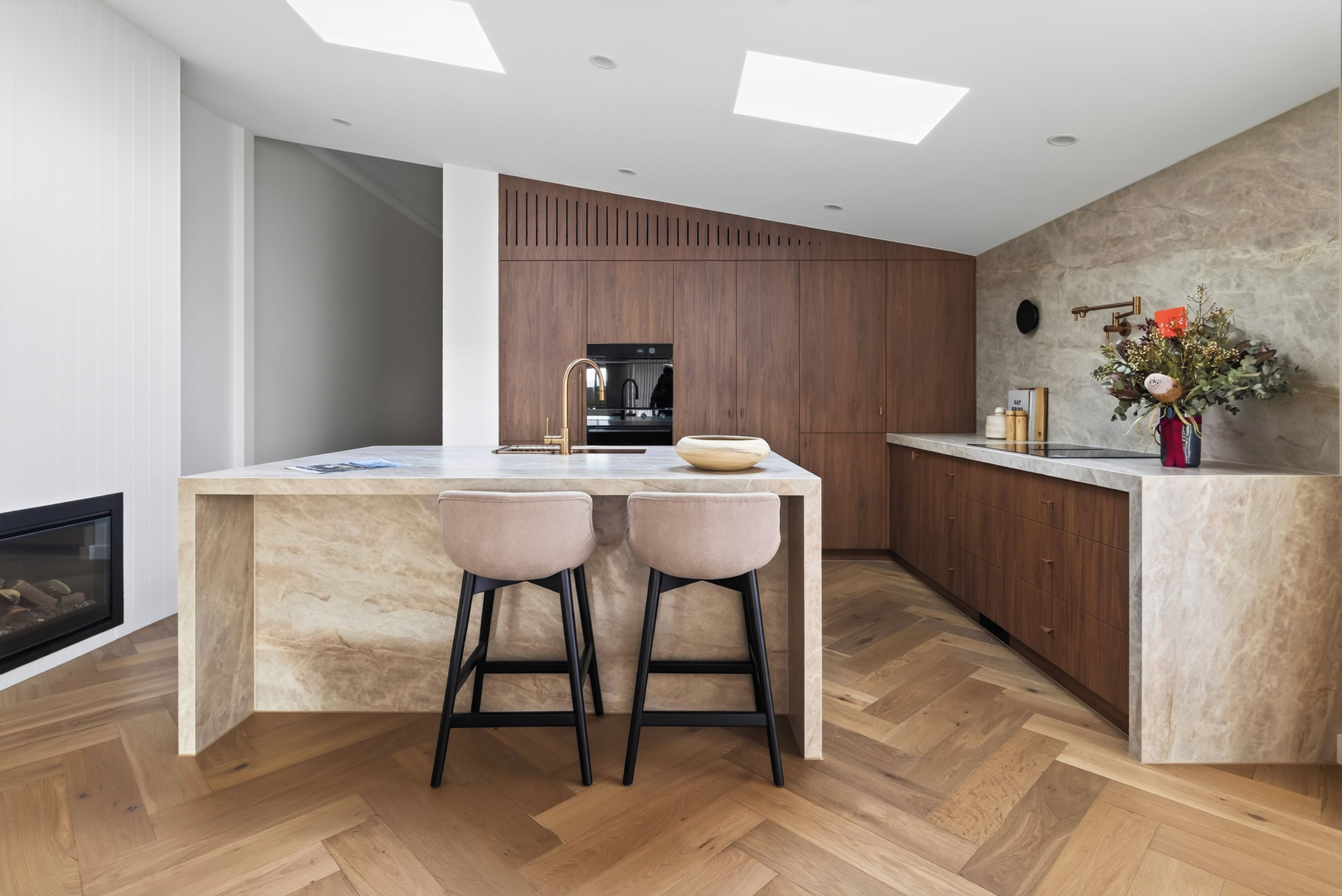 A modern kitchen with a central island, bar stools, a built-in oven, and a stone wall.