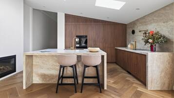 A modern kitchen with a central island, bar stools, a built-in oven, and a stone wall.