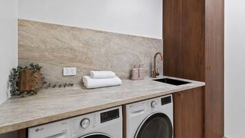A laundry area with a washing machine, dryer, and a sink with a faucet. There are towels stacked on the counter and a potted plant.