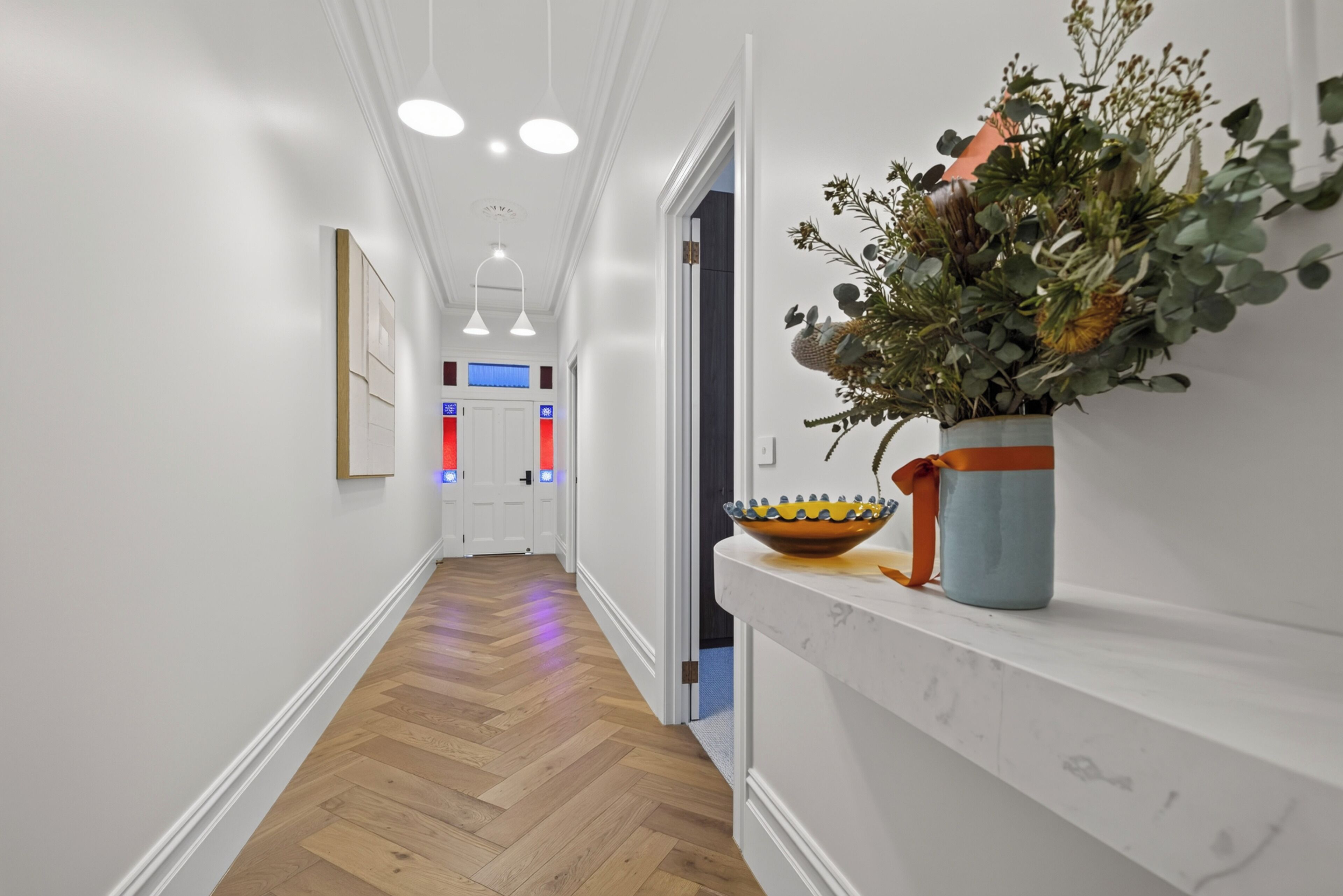 A hallway with wooden flooring, white walls, and a plant on a shelf.