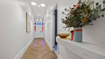 A hallway with wooden flooring, white walls, and a plant on a shelf.