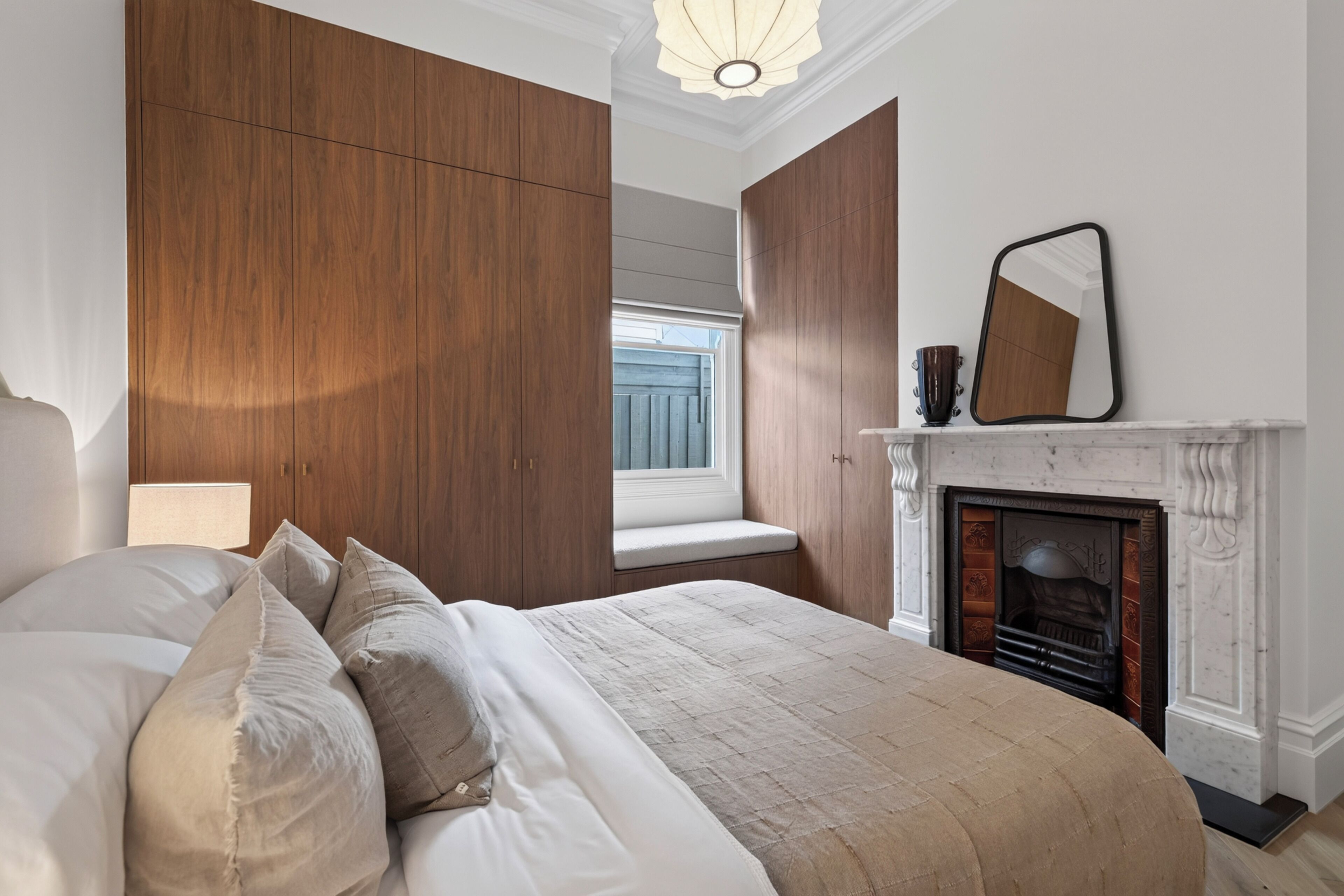 A bedroom with a large bed, wooden wardrobe, a fireplace, and a window.