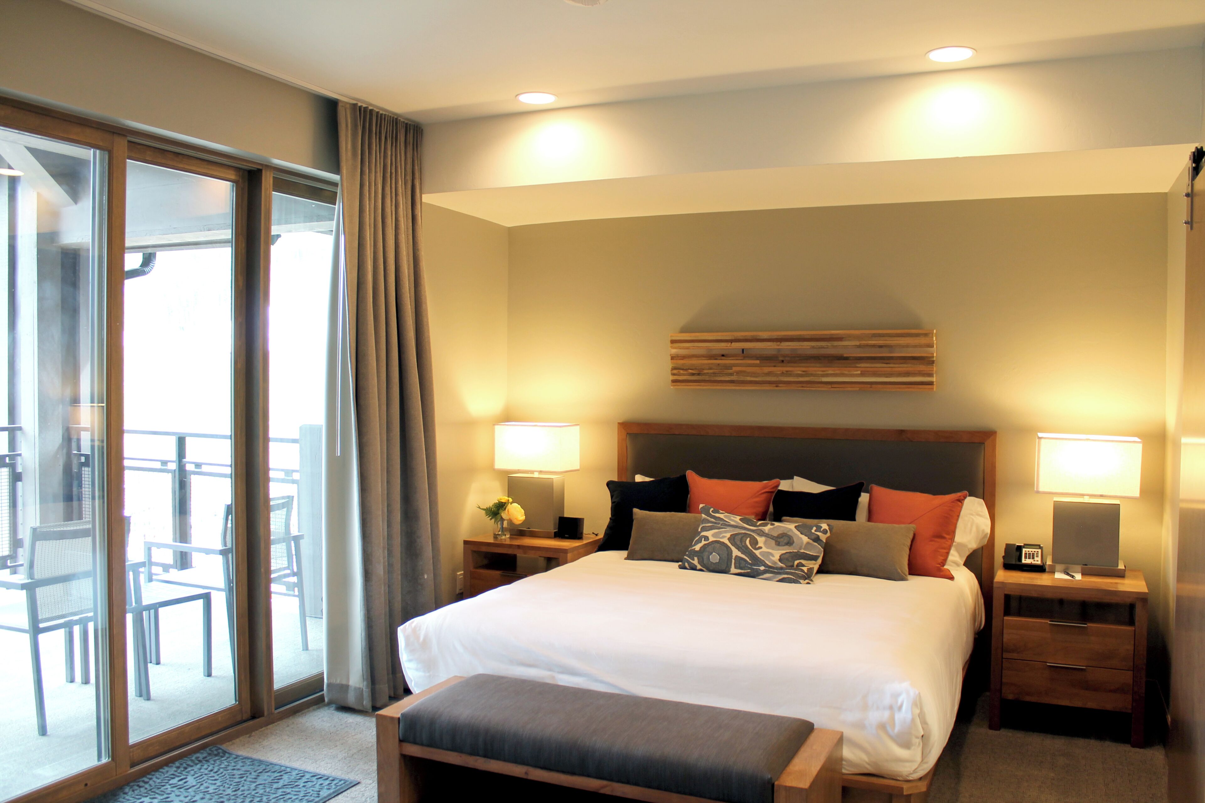 A hotel room with a large bed, two bedside tables, a wooden headboard, and a balcony with chairs.