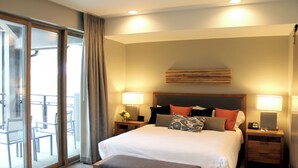 Een hotelkamer met een groot bed, twee nachtkastjes, een houten hoofdbord en een balkon met stoelen.