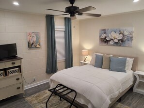 Ein Schlafzimmer mit einem Bett, einem Fernseher auf einer Kommode, einem Deckenventilator, einem Gemälde und einer Lampe.