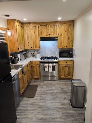 A compact kitchen with wooden cabinets, a stainless steel stove, a microwave, and a trash bin. - Slip Away to Honeysuckle Hideaway! Free Wine & 5 off Horse Drawn Carriage Ride (Natchez)