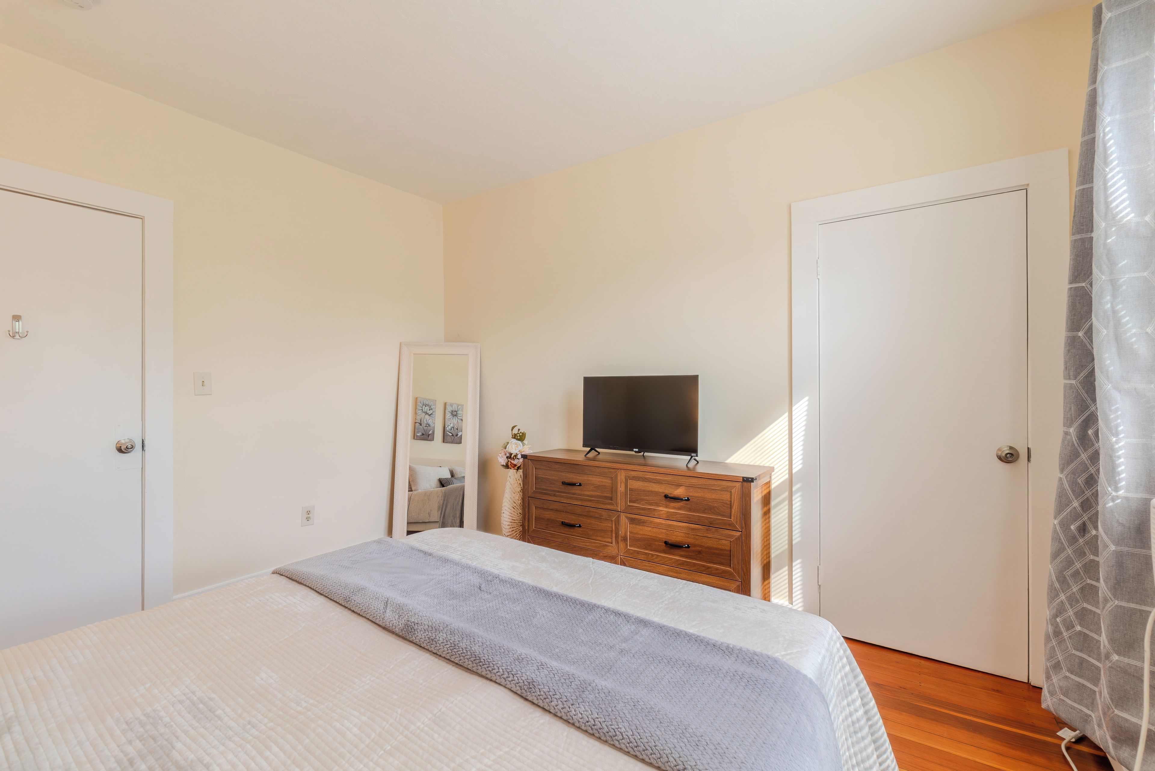 A bedroom with a bed, a dresser, a television, and two doors.