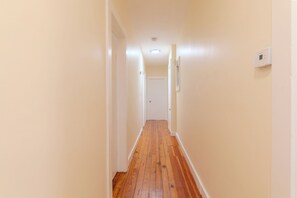 A narrow hallway with wooden flooring, white walls, and a door at the end. - NEW - Boston/Cambridge/3BR/Near MIT + Newbury St (Cambridge)