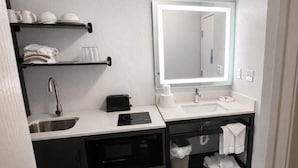 A modern bathroom with a sink, mirror, and built-in microwave. - 2 Convenient Rooms w/ Kitchen for Group Stays Near Outlets of Des Moines -1.3 mi (Altoona)