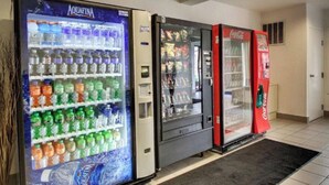 A row of vending machines with various beverages, including Aquafina water, in a hallway. - 2 Convenient Rooms w/ Kitchen for Group Stays Near Outlets of Des Moines -1.3 mi (Altoona)