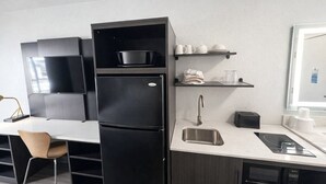 Une cuisine moderne dotée d’un réfrigérateur noir encastré, d’un évier en acier inoxydable et d’un plan de travail sur lequel se trouvent un grille-pain et une bouilloire.
