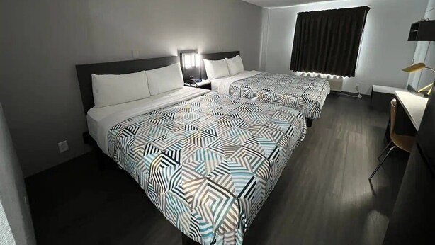 Une chambre d’hôtel avec deux lits, un bureau, une chaise, une fenêtre avec des rideaux et une lampe.