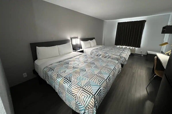Ein Hotelzimmer mit zwei Betten, einem Schreibtisch, einem Stuhl, einem Fenster mit Vorhängen und einer Lampe.