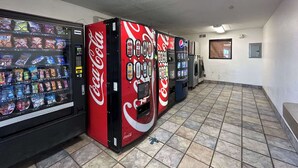 A row of vending machines with Coca-Cola branding, a tiled floor, and a plain wall with a door. - Enjoy a Convenient Kitchen-Equipped Stay for Longer Comfort | Free Parking (Lubbock)