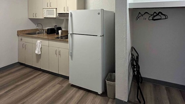 A compact kitchen with a refrigerator, microwave, and sink. There is a towel hanging on the cabinet door. - Enjoy a Convenient Kitchen-Equipped Stay for Longer Comfort | Free Parking (Lubbock)