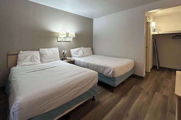 Ein Hotelzimmer mit zwei Betten, einem Nachttisch mit Telefon und einem Kleiderständer.