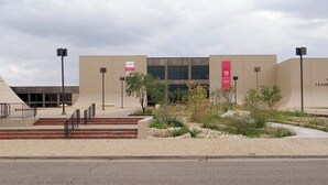Un bâtiment moderne doté d’un toit plat, d’une grande entrée avec des marches et d’une enseigne indiquant une réduction de 90 %.