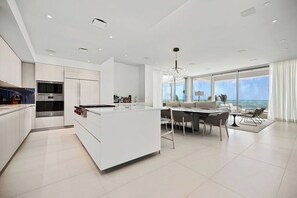 A modern kitchen with a central island, stainless steel appliances, and a dining area with a view of the sea. - Amazing Four Seasons Beachfront 4BR Residence - Golf Cart Included (Río Grande)